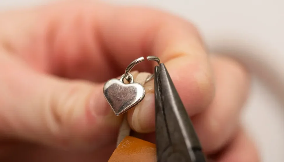 Relicário de cinzas personalizado em formato de colar, com acabamento em prata, sobre superfície de madeira clara