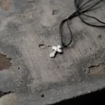 Pingente de cruz prateada sobre pedra rústica, representando joias para cinzas de pet e acessórios de memória para luto.