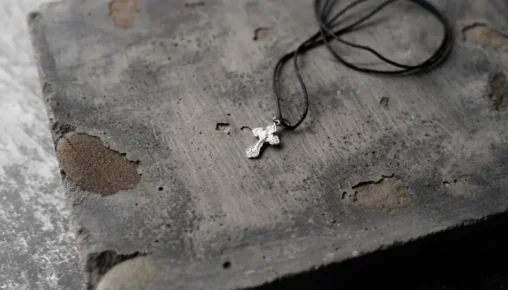 Pingente de cruz prateada sobre pedra rústica, representando joias para cinzas de pet e acessórios de memória para luto.