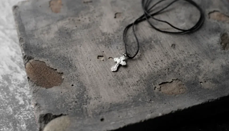 Pingente de cruz prateada sobre pedra rústica, representando joias para cinzas de pet e acessórios de memória para luto.